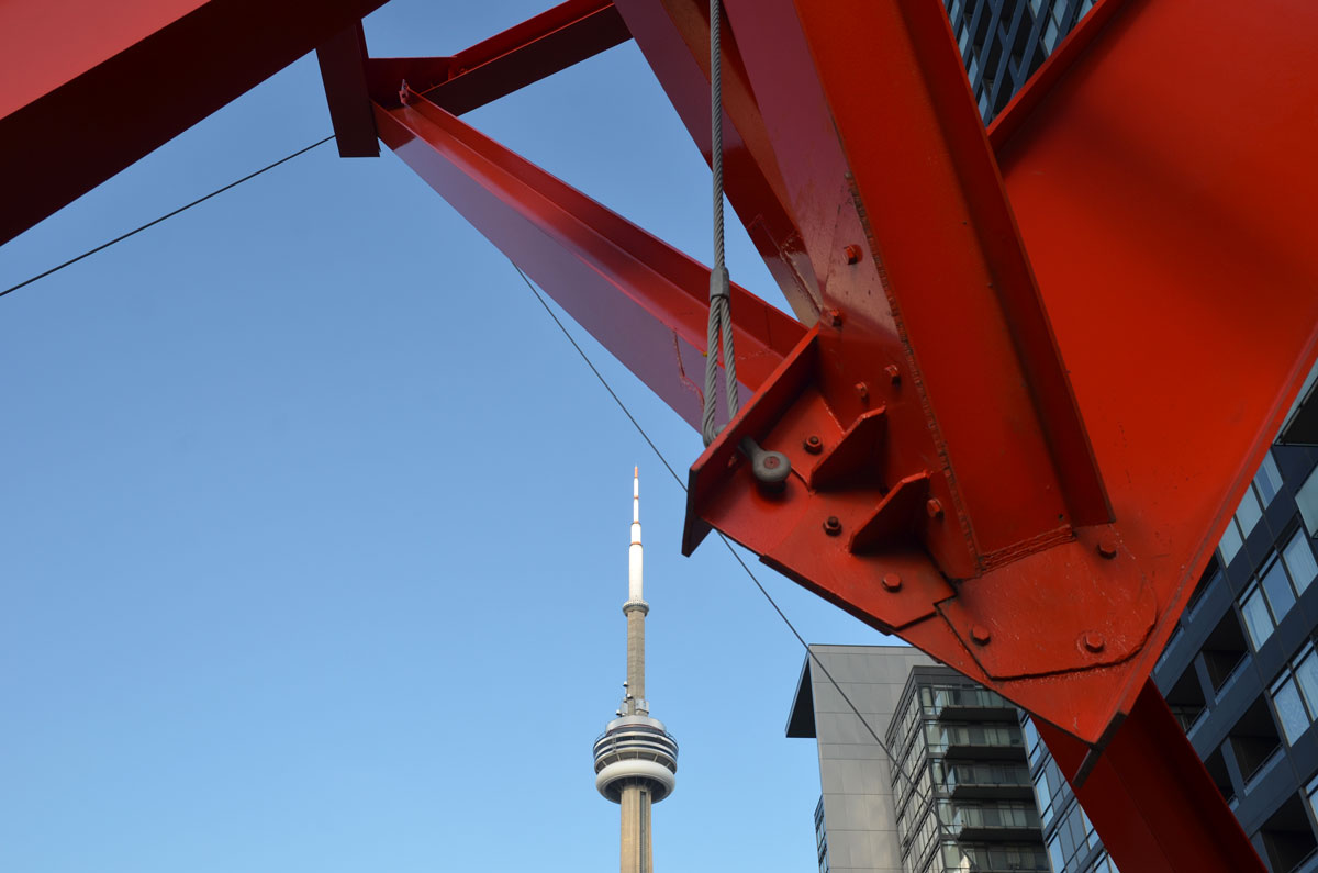 the CN tower is in the distance but it looks like it is under a large red metal sculpture.  