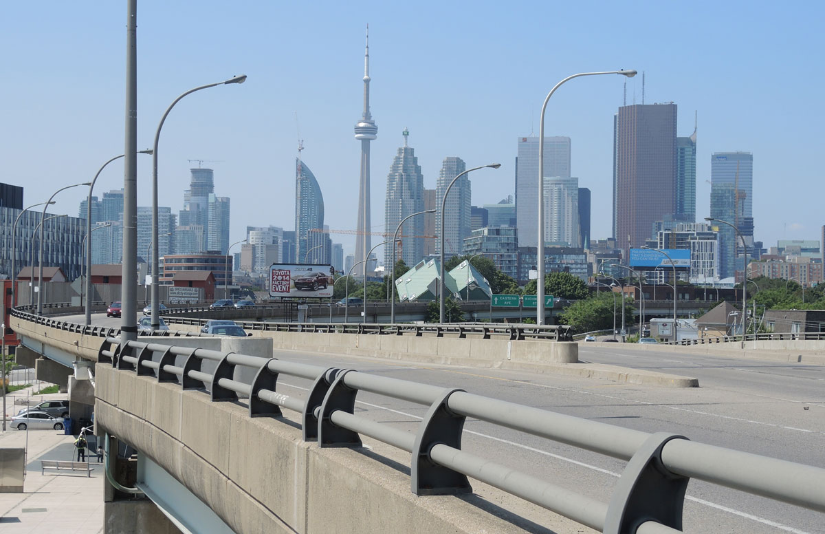 looking along a ramp of a main road, with the CN tower and the Toronto skyline in the hazy background.  
