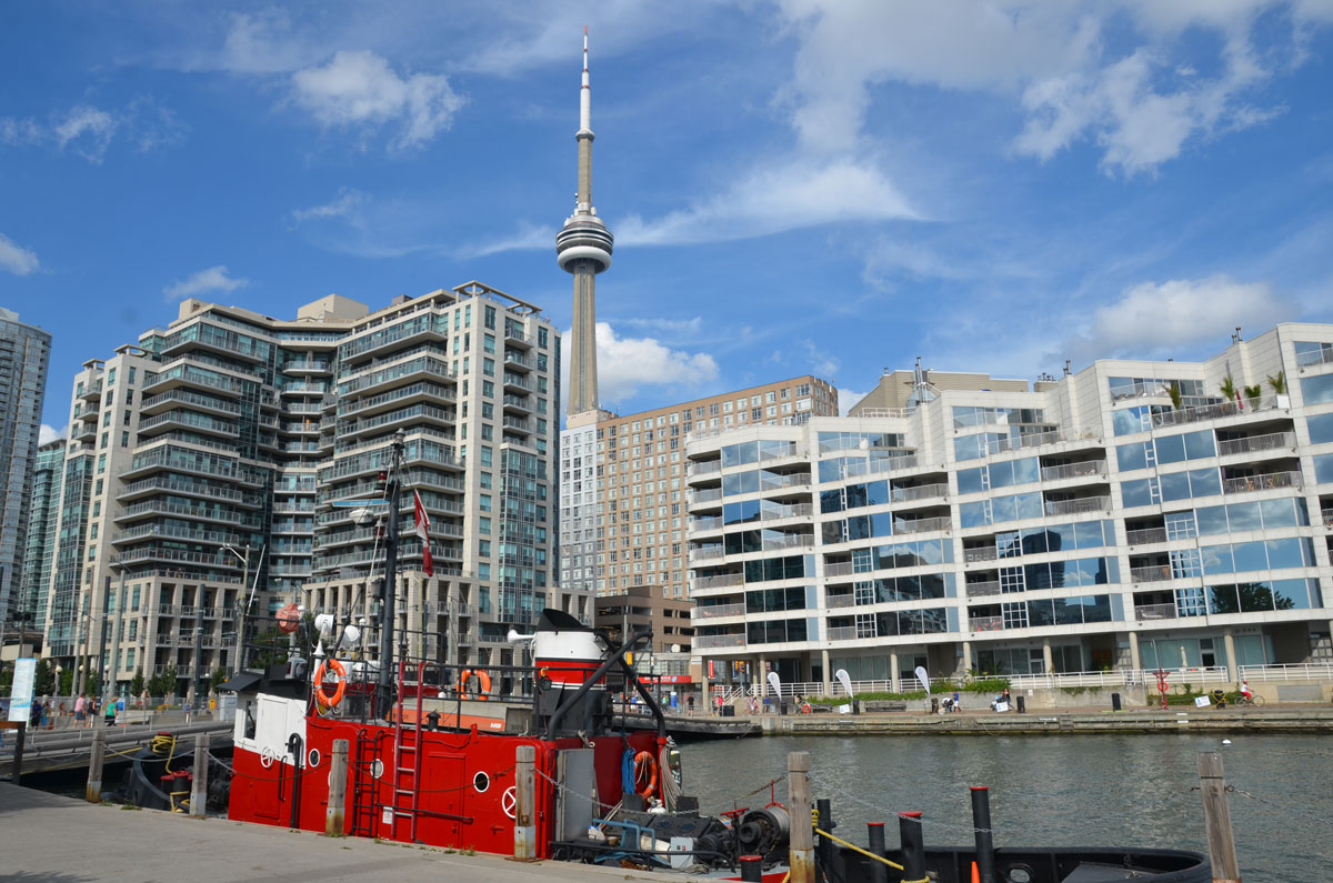 a red and white tug boat is moored on the TOronto waterfront, with the CN tower in the background.  