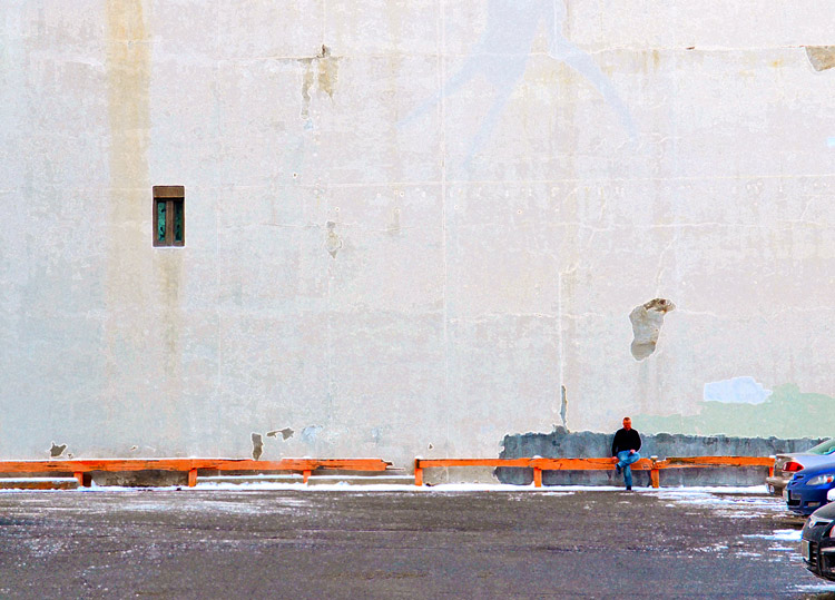  a man sitting on a guardrail at the edge of a parking lot