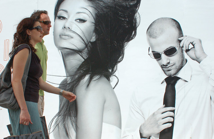 a couple walking past a billboard featuring large pictures of a man and a woman