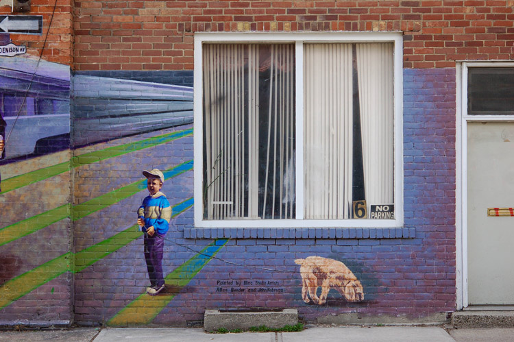 a window with white vertical blinds on a wall that has a mural of a boy and his dog