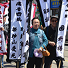 a group of Chinese people in a small parade.  They are all holding white banners with either red or blue Chinese characters on them. 
