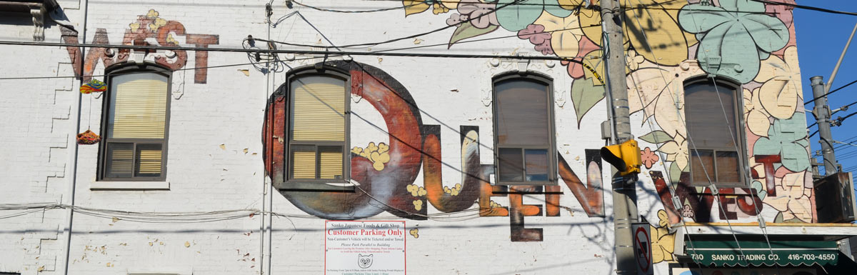 large painted letters on the side of a white brick building that say West Queen West