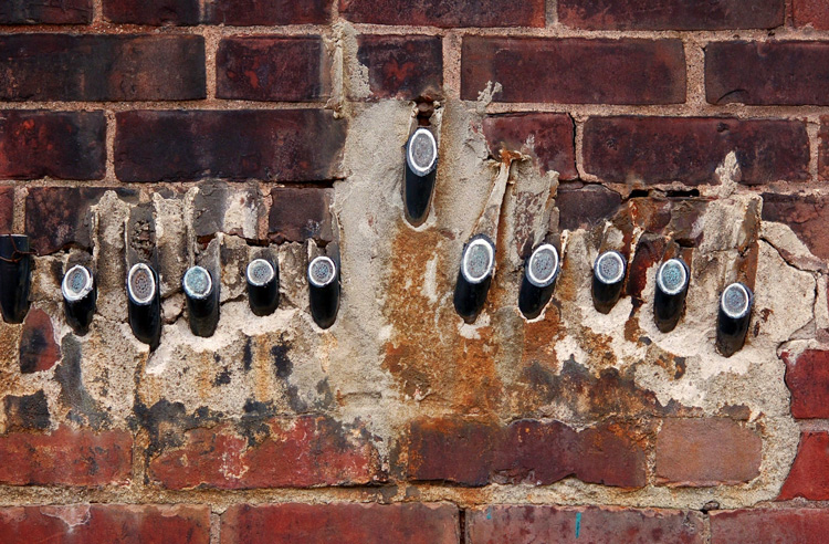 ten cables that have been cut close to a the brick wall that they are coming out of