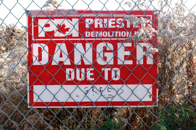 red and white construction sign that has been altered to say danger due to greed