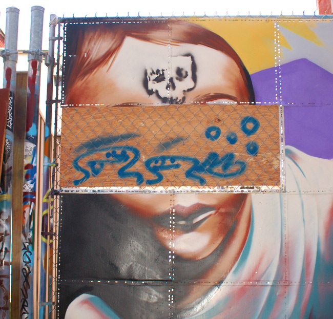 graffiti of a face on a gate that has had part removed