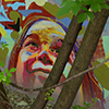 graffiti on a concrete walll behind some young trees.   A colourful face