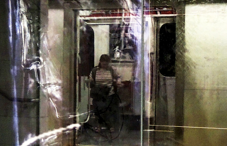 a woman is sitting on a subway car when it is stopped at Union station, the door of the car is open, and this scene is reflected in the glass panels of the art on the wall at the station. 