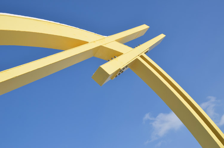 close up shot of the yellow arches of a bridge support against the blue sky.  