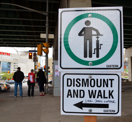 walk sign that has been altered to read, walk like John Wayne