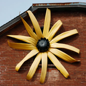large metal black eyed susan flower on the side of a brick building