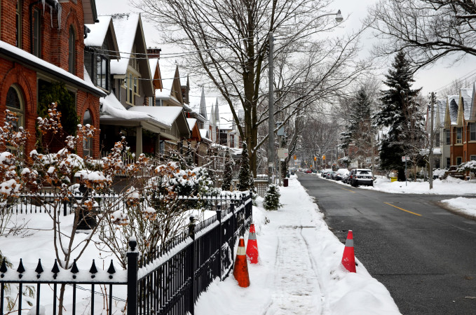 a view of a residential street in the winter with snow on sidewalks, wrought iron fence in the foreground.