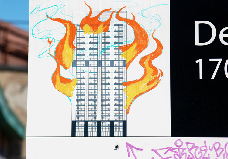 Someone has added orange and yellow flames to the drawing of a building on a standard Development Proposal sign for the City of Toronto. 