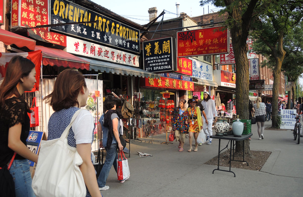 two Asian women in the foreground, walking past Chinese shops on Spadina in Toronto's Chinatown. 