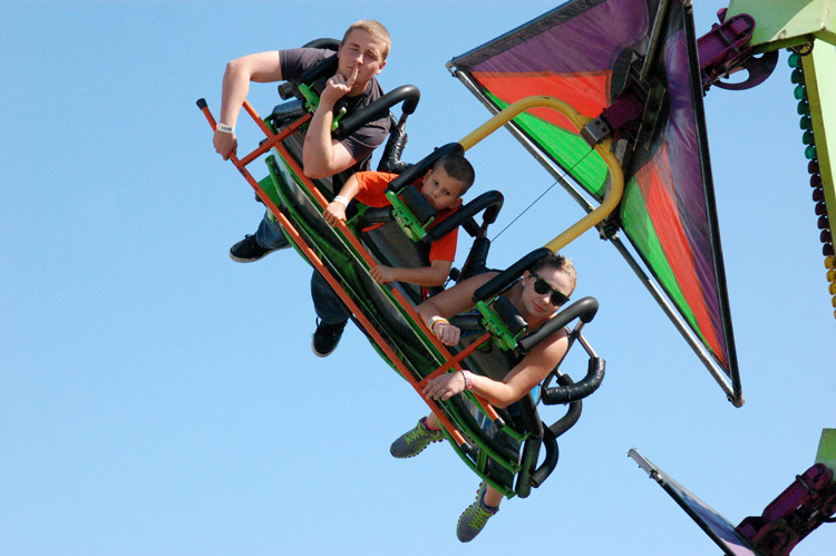 three riders on a midway ride.  One is pretending to be contemplating the world in stead of getting excited about being on the ride.