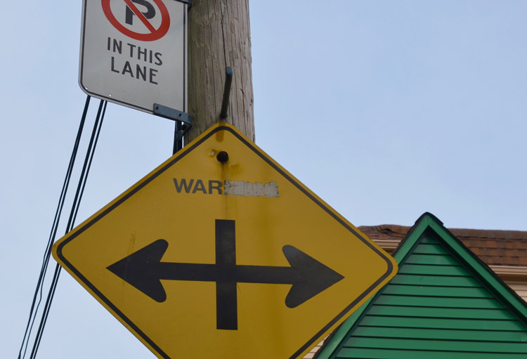 road sign with the word warning altered to say war