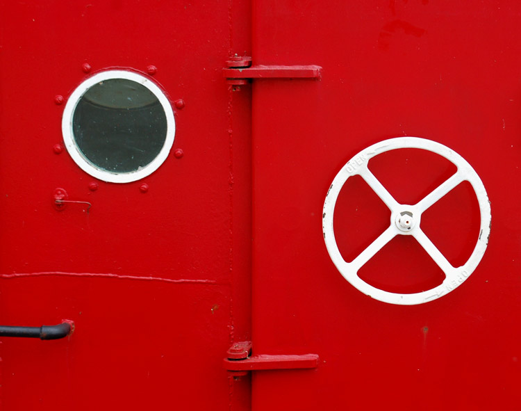 white wheel and a white rimmed porthole on the side of a red boat